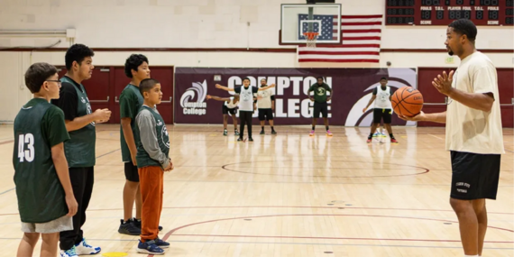 Coach demonstrates basketball drill to young players at Compton College gym