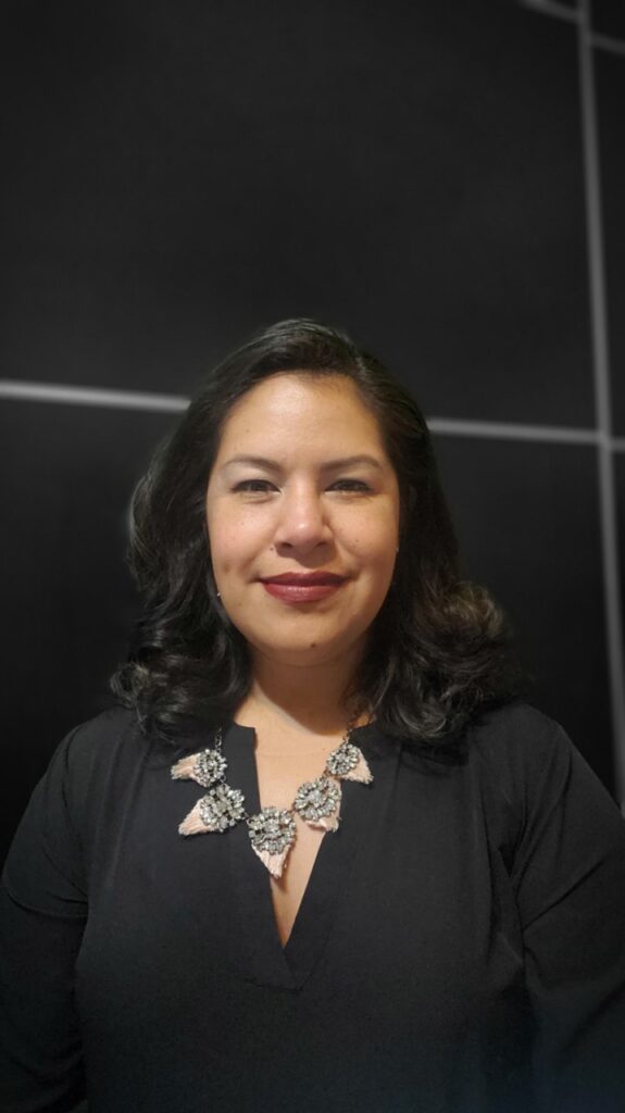 Woman in a black top and statement necklace smiles at the camera