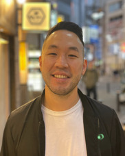 Man with short dark hair smiling in front of a blurred city street
