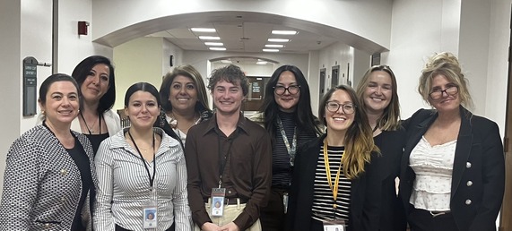 Group of 9 people posing for a photo in a hallway.